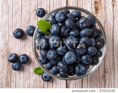 Sweet blueberries in a glass bowl over wooden surface. 97650286