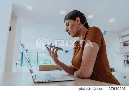 Woman sitting in living room using laptop and smartphone look at cam talk by video call with business friend relatives, head shot. Job interview answering questions. Woman sitting in living room using laptop and smartphone look at cam talk by video call with business friend relatives, head shot. Job interview answering questions. 97650292