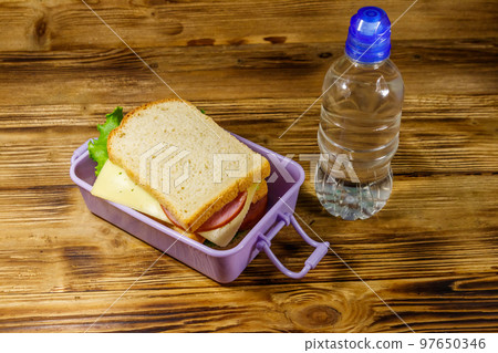 Lunch box with sandwiches and bottle of water on a wooden table 97650346