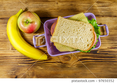 Lunch box with sandwiches, banana and apple on a wooden table. Top view Lunch box with sandwiches, banana and apple on a wooden table. Top view 97650352
