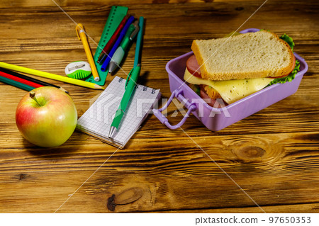 Back to school concept. School supplies, apple and lunch box with sandwiches on a wooden desk Back to school concept. School supplies, apple and lunch box with sandwiches on a wooden desk 97650353