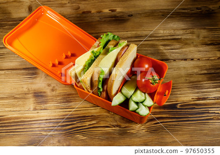 Lunch box with sandwiches and fresh vegetables on a wooden table 97650355