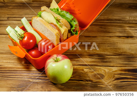 Apple and lunch box with sandwiches and fresh vegetables on a wooden table Apple and lunch box with sandwiches and fresh vegetables on a wooden table 97650356
