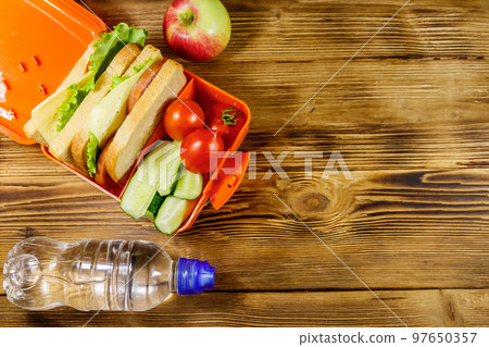 Bottle of water, apple and lunch box with sandwiches and fresh vegetables on a wooden table. Top view, copy space 97650357
