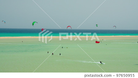 Group of kite surfer kiteboarding on waves of Atlantic Ocean in Playa Esmeralda, Fuerteventura, Canary Islands, Spain. Azure calm ocean waves. Picteresque spectacular cinematic. Slow motion. Group of kite surfer kiteboarding on waves of Atlantic Ocean in Playa Esmeralda, Fuerteventura, Canary Islands, Spain. Azure calm ocean waves. Picteresque spectacular cinematic. Slow motion. 97650955