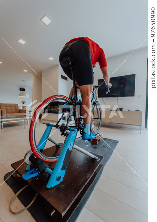 A man riding a triathlon bike on a machine simulation in a modern living room. Training during pandemic conditions. A man riding a triathlon bike on a machine simulation in a modern living room. Training during pandemic conditions. 97650990