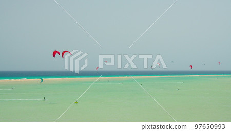 Costa Calma, Fuerteventura. Free kiters on the ocean waves. Kitesurfing in the shallow blue transparent water. Paradise island. Sport activity. Large group of athletes. Costa Calma, Fuerteventura. Free kiters on the ocean waves. Kitesurfing in the shallow blue transparent water. Paradise island. Sport activity. Large group of athletes. 97650993