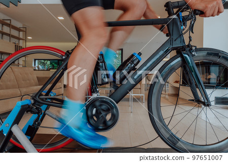 A man riding a triathlon bike on a machine simulation in a modern living room. Training during pandemic conditions. 97651007
