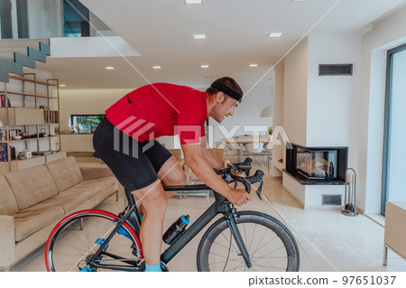 A man riding a triathlon bike on a machine simulation in a modern living room. Training during pandemic conditions. 97651037