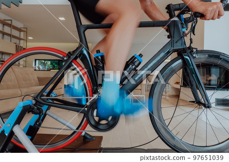 A man riding a triathlon bike on a machine simulation in a modern living room. Training during pandemic conditions. A man riding a triathlon bike on a machine simulation in a modern living room. Training during pandemic conditions. 97651039