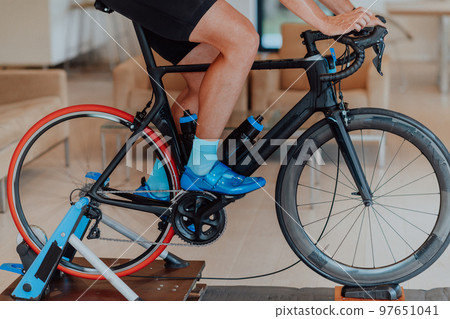 A man riding a triathlon bike on a machine simulation in a modern living room. Training during pandemic conditions. A man riding a triathlon bike on a machine simulation in a modern living room. Training during pandemic conditions. 97651041