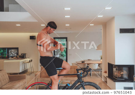 A man riding a triathlon bike on a machine simulation in a modern living room. Training during pandemic conditions. A man riding a triathlon bike on a machine simulation in a modern living room. Training during pandemic conditions. 97651043
