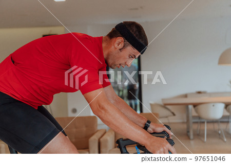 A man riding a triathlon bike on a machine simulation in a modern living room. Training during pandemic conditions. A man riding a triathlon bike on a machine simulation in a modern living room. Training during pandemic conditions. 97651046