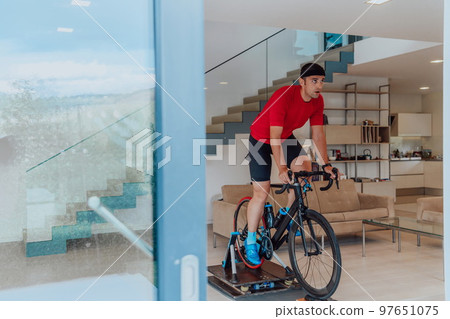 A man riding a triathlon bike on a machine simulation in a modern living room. Training during pandemic conditions. A man riding a triathlon bike on a machine simulation in a modern living room. Training during pandemic conditions. 97651075