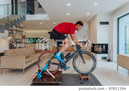 A man riding a triathlon bike on a machine simulation in a modern living room. Training during pandemic conditions. A man riding a triathlon bike on a machine simulation in a modern living room. Training during pandemic conditions. 97651104