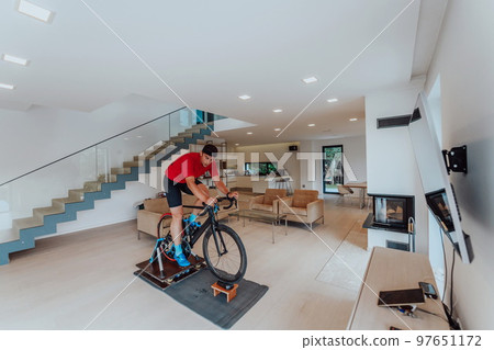 A man riding a triathlon bike on a machine simulation in a modern living room. Training during pandemic conditions. A man riding a triathlon bike on a machine simulation in a modern living room. Training during pandemic conditions. 97651172