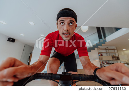 A man riding a triathlon bike on a machine simulation in a modern living room. Training during pandemic conditions. A man riding a triathlon bike on a machine simulation in a modern living room. Training during pandemic conditions. 97651180