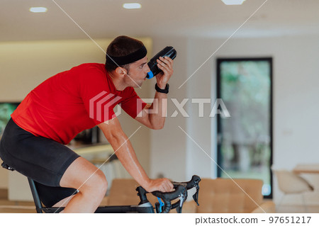 A man riding a triathlon bike on a machine simulation in a modern living room. Training during pandemic conditions. A man riding a triathlon bike on a machine simulation in a modern living room. Training during pandemic conditions. 97651217