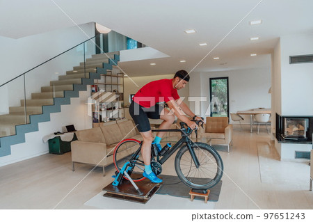 A man riding a triathlon bike on a machine simulation in a modern living room. Training during pandemic conditions. A man riding a triathlon bike on a machine simulation in a modern living room. Training during pandemic conditions. 97651243