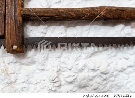 Old antique saw with wooden handle on the white wall Old antique saw with wooden handle on the white wall 97652122