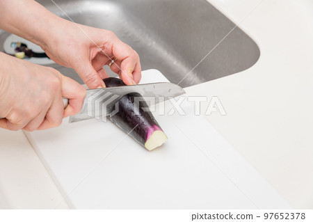 [A middle-aged housewife cuts an eggplant into strips with a Santoku knife] 97652378