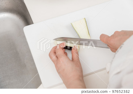 [A middle-aged housewife cuts an eggplant into strips with a Santoku knife] 97652382