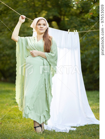 Pretty pregnant woman with big belly stands near clothesline with bed sheet, young girl takes care of sensitive skin's microbiome, holds hand on tummy outside in sunny day, looking away.Vertical Pretty pregnant woman with big belly stands near clothesline with bed sheet, young girl takes care of sensitive skin's microbiome, holds hand on tummy outside in sunny day, looking away.Vertical 97653009