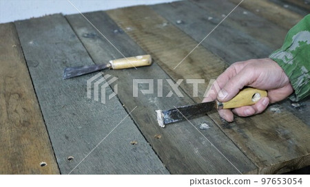 smearing nail marks on a wooden shelf or table from old textured darkened boards with a narrow spatula and mastic, applying a plastic solution to a cracked wooden surface 97653054