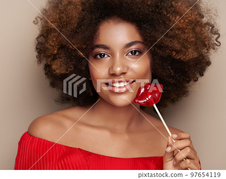 Beautiful portrait of an African girl with a lips shaped lollipop Beautiful portrait of an African girl with a lips shaped lollipop 97654119