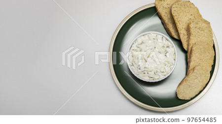 Traditional homemade greek yogurt sauce Tzatziki, tarator in white bowl, made of grated cucumbers, sour cream yogurt,olive oil,garlic,herbs on plate with sliced bread. Copy space. Horizontal Traditional homemade greek yogurt sauce Tzatziki, tarator in white bowl, made of grated cucumbers, sour cream yogurt,olive oil,garlic,herbs on plate with sliced bread. Copy space. Horizontal 97654485