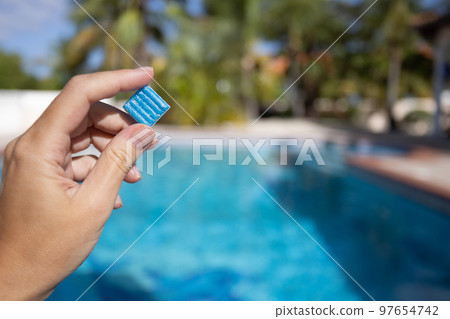Hand holding small blue tile from floor of swimming pool. Maintenance of the swimming pool. 97654742