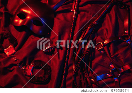 Erotic sex toys for adults for BDSM sex with submission and domination. Handcuffs, mask and leather flogger whip on a black background 97658974