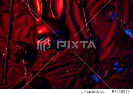 Erotic sex toys for adults for BDSM sex with submission and domination. Handcuffs, mask and leather flogger whip on a black background 97658975