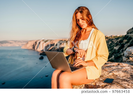 Digital nomad, Business woman working on laptop by the sea. Pretty lady typing on computer by the sea at sunset, makes a business transaction online from a distance. Freelance, remote work on vacation Digital nomad, Business woman working on laptop by the sea. Pretty lady typing on computer by the sea at sunset, makes a business transaction online from a distance. Freelance, remote work on vacation 97663458