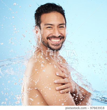 Portrait, water and shower with a man model in studio on a blue background for hygiene or hydration. Face, beauty and skincare with a handsome young male wet from a water splash in the bathroom 97663918