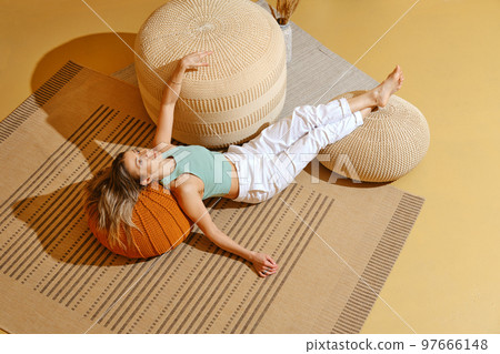 Senior woman is lying on the floor with her legs on padded stool in relaxing environment Senior woman is lying on the floor with her legs on padded stool in relaxing environment 97666148