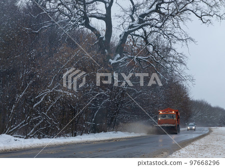 A large car with a plow clears the road from snow. Orange cargo special equipment is struggling with the elements in winter. Removing the effects of the snowstorm. Difficulties in traffic.Frozen water 97668296