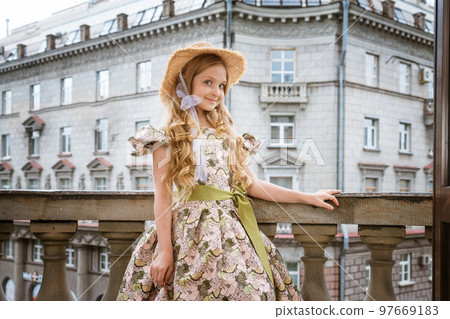 Little girl in dress and hat posing on the balcony 97669183