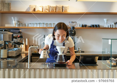 Smiling asian girl barista, working in cafe, brewing coffee v60, preparing order behind counter 97669768