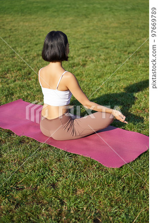 Rear view of woman silhouette doing yoga, sitting on fitness mat and meditating on green lawn 97669789