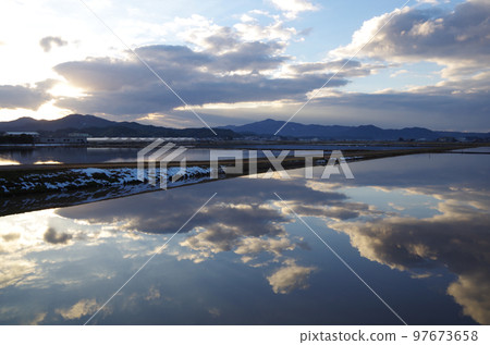A composition in which the winter rice field in the windless evening reflects the winter blue sky and clouds like a large mirror 97673658