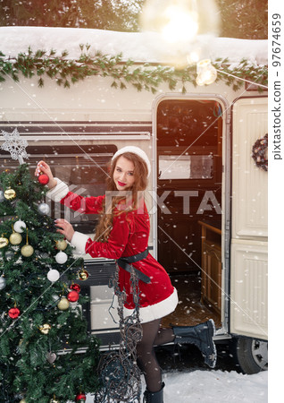 Young woman in santa costume decorates the Christmas tree at winter campsite 97674659