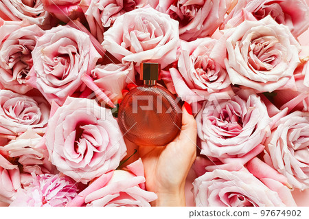 Unbranded brown round perfume bottle in female hand and pink rose flowers background. Transparent glass perfume bottle for branding and label. Eau de toilette. Mockup, summer flat lay. Unbranded brown round perfume bottle in female hand and pink rose flowers background. Transparent glass perfume bottle for branding and label. Eau de toilette. Mockup, summer flat lay. 97674902