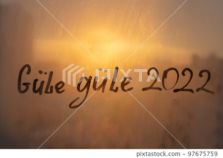 lettering Gule Gule in Turkish is goodbye in english and numbers 2022 paint with finger of water on splashed by frost foggy glass on sunset window 97675759