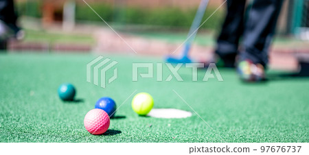 Mini golf game with several colored balls in the way of a putter lined up. Mini golf game with several colored balls in the way of a putter lined up. 97676737