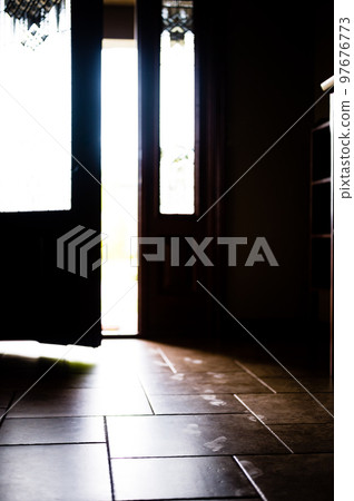 Track of small child footprints visible on a tile floor with an open door letting in light in the background 97676773
