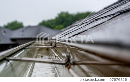Selective focus on a section of residential guttering with hanger conveying water during a storm. Rain splatters and drops visible. 97676826