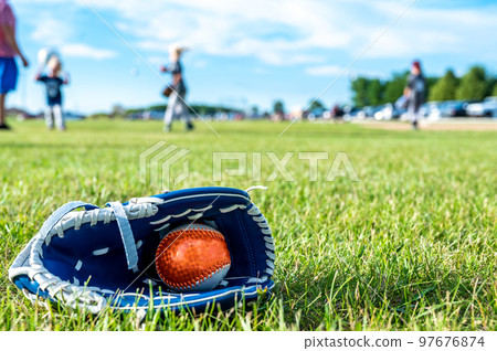 T-ball resting inside a baseball glove on grass. Defocused players in background 97676874