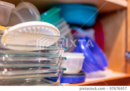 Narrow depth of field picture of an open kitchen cabinet with an assortment of containers and mismatched lids stacked. 97676957