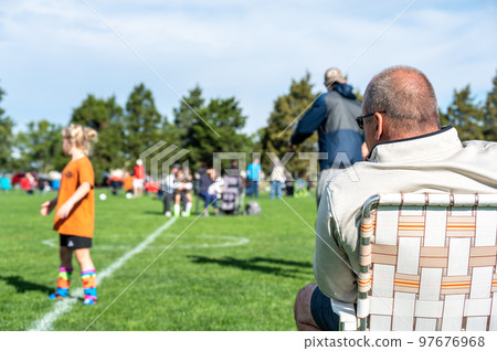 Grandpa watching his granddaughter playing soccer on a fall afternoon. Grandpa watching his granddaughter playing soccer on a fall afternoon. 97676968